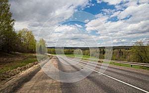 A Deserted country road along the forest under blue sky with clouds