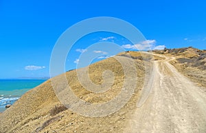 Deserted dirt road on a promontory towards the sea and lonely beach in summer day