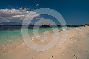 Deserted island coast scene in bright afternoon rock formation island in the ocean footsteps on the beach sand. Sumbawa