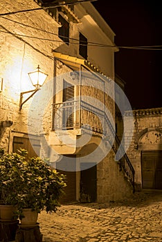 Deserted street with stone house with stairs and paved sidewalk in medeival historical part of Trogir city, Croatia lit by