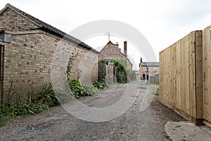 Deserted village side street showing old buildings to the left and a newly installed garden fence on the right.