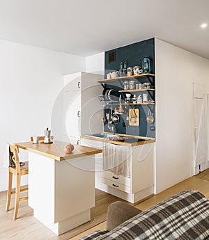 Design of modern home kitchen in the attic and rustic style. Black wall with shelves, trays, jars, mugs. Refrigerator, dining tabl