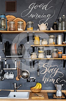 Design of modern stylish home kitchen in rustic loft style and. Black chalk wall with shelves, trays, jars, mugs, sink,