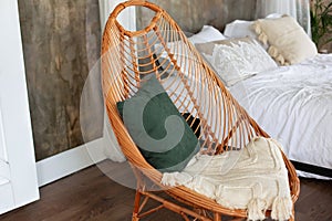 Design wicker wooden chair with pillows in stylish light bedroom interior. Modern Rattan armchair in the living room.