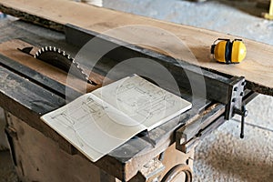 Design wood small business concept. Technical drawing in notebook lying on top of wood in garage or workroom near yellow headset