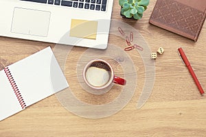 For design wooden office desk table with notebook, laptop, glasses, plant, red cup of cappuccino and other office supplies. Top vi