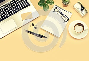 For design yellow office table with laptop, green plants, pens, glasses, camera and cup of coffee. Top view with copy space, flat