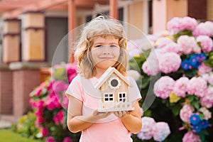 Design of your dream house. Kid playing with small house model outdoors at home garden.