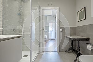 Designer bathroom with marble sink under wall-mounted mirror and shower with tempered glass partitions and access door to an en-