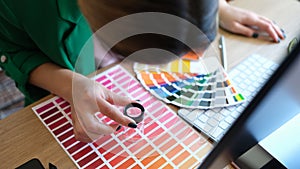 Designer looks through magnifying glass at samples of colors and shades of red on paper palette