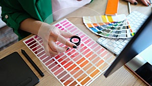 Designer with magnifying glass works with pantone scale in art studio.