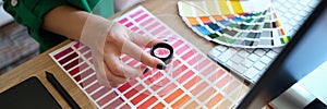 Designer with magnifying glass works with pantone scale in art studio.