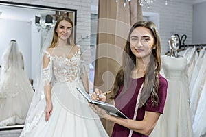 Designer with notepad and bride in wedding dress behind