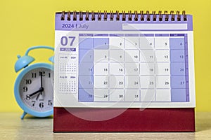 Desk calendar for July 2024 on the table next to the alarm clock