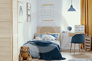 Desk, chair and single bed with blue bedding in cozy bedroom interior for children