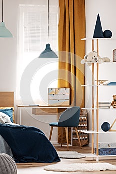 Desk, chair and single bed with blue bedding in cozy bedroom interior for children