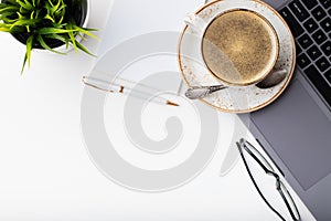 Desk with laptop, eye glasses, notepad, pen and a cup of coffee on a white table. Top view with copy space. Flat lay. Light backgr