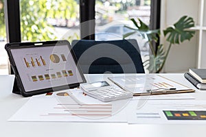 A desk in the office of the finance department, on the table there is a tablet on the screen showing a financial summary chart and