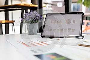 A desk in the office of the finance department, on the table there is a tablet on the screen showing a financial summary chart and