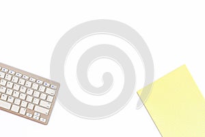 Desk in the office with a keyboard and a yellow Notepad on a white background. Top view with copy space.