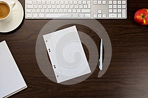 Desk in the office with note and pen, a keyboard next to a cup o