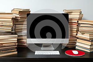 Desk top computer surrounded with stacks of books on the table. Concept of studying online and preparing for exams