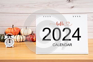 The Desktop calendar for 2024 year and heap pumpkins with clock on wooden table