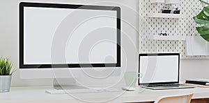 Desktop computer and blank screen laptop with copy space and office supplies in minimal white office room