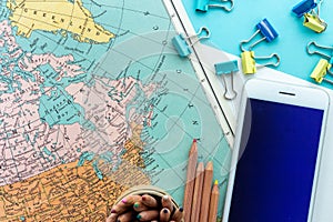 Desktop design of Map of Canada, Greenland and the North of America with colorful paperclips, colored pencils and mobile phone