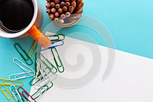 Desktop design with orange mug of coffee, colorful paperclips and colored pencils