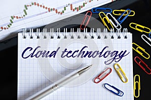 On the desktop are a forex chart, paper clips, a pen and a notebook in which it is written - Cloud technology