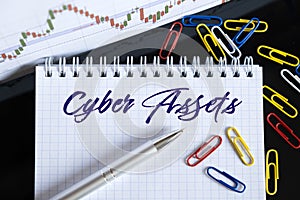 On the desktop are a forex chart, paper clips, a pen and a notebook in which it is written - Cyber Assets