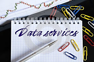 On the desktop are a forex chart, paper clips, a pen and a notebook in which it is written - Data services