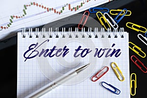 On the desktop are a forex chart, paper clips, a pen and a notebook in which it is written - Enter to win