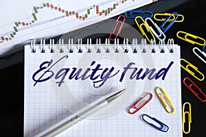 On the desktop are a forex chart, paper clips, a pen and a notebook in which it is written - Equity fund