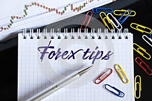On the desktop are a forex chart, paper clips, a pen and a notebook in which it is written - Forex tips