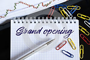 On the desktop are a forex chart, paper clips, a pen and a notebook in which it is written - Grand opening