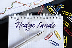 On the desktop are a forex chart, paper clips, a pen and a notebook in which it is written - Hedge funds