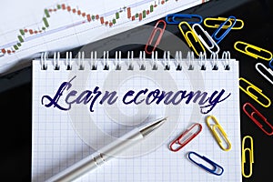 On the desktop are a forex chart, paper clips, a pen and a notebook in which it is written - Learn economy