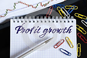 On the desktop are a forex chart, paper clips, a pen and a notebook in which it is written - Profit growth