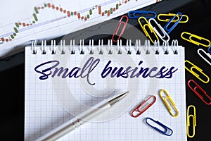On the desktop are a forex chart, paper clips, a pen and a notebook in which it is written - Small business