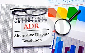 On the desktop are glasses, a magnifying glass, color charts and a white notebook with the text ADR Alternative Dispute Resolution