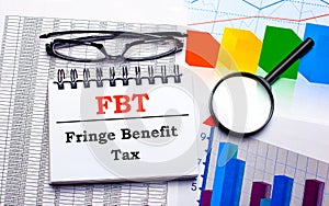 On the desktop are glasses, a magnifying glass, color charts and a white notebook with the text FBT Fringe Benefit Tax. Business