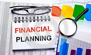 On the desktop are glasses, a magnifying glass, color charts and a white notebook with the text FINANCIAL PLANNING. Business