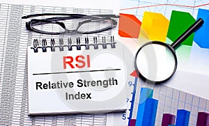 On the desktop are glasses, a magnifying glass, color charts and a white notebook with the text RSI Relative Strength Index.