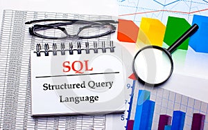 On the desktop are glasses, a magnifying glass, color charts and a white notebook with the text SQL Structured Query Language.