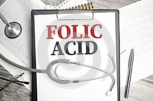 The desktop has a stethoscope, a blue pen, and a gray file folder with the text FOLIC ACID