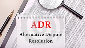 Desktop magnifier, reports, pen and notebook with text ADR Alternative Dispute Resolution. Business concept