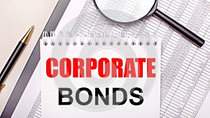 Desktop magnifier, reports, pen and notebook with text CORPORATE BONDS. Business concept