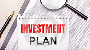 Desktop magnifier, reports, pen and notebook with text INVESTMENT PLAN. Business concept